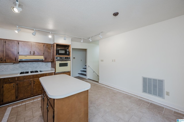 kitchen featuring white appliances, a textured ceiling, a center island, and backsplash