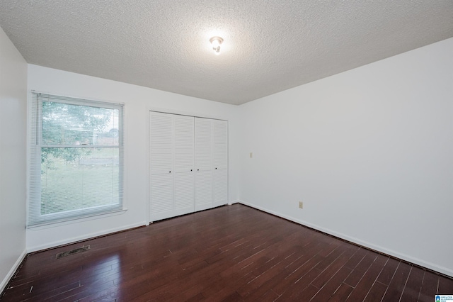 unfurnished bedroom featuring a textured ceiling, dark wood-type flooring, and a closet