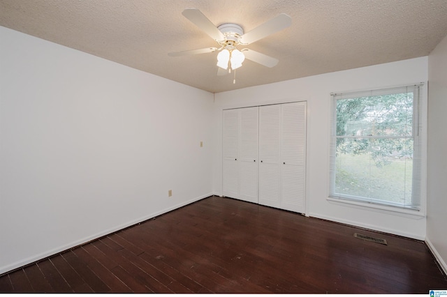 unfurnished bedroom featuring ceiling fan, a closet, dark wood-type flooring, and a textured ceiling