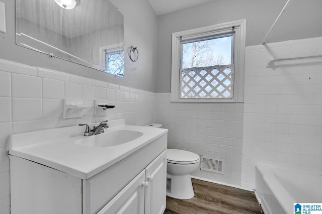 bathroom featuring a tub to relax in, hardwood / wood-style floors, toilet, vanity, and tile walls