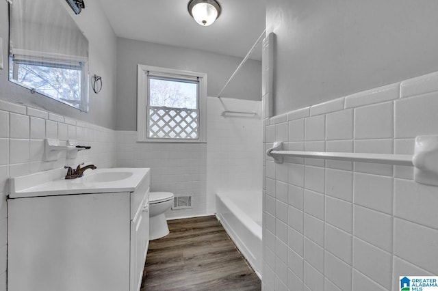 full bathroom with bathing tub / shower combination, hardwood / wood-style floors, toilet, vanity, and tile walls