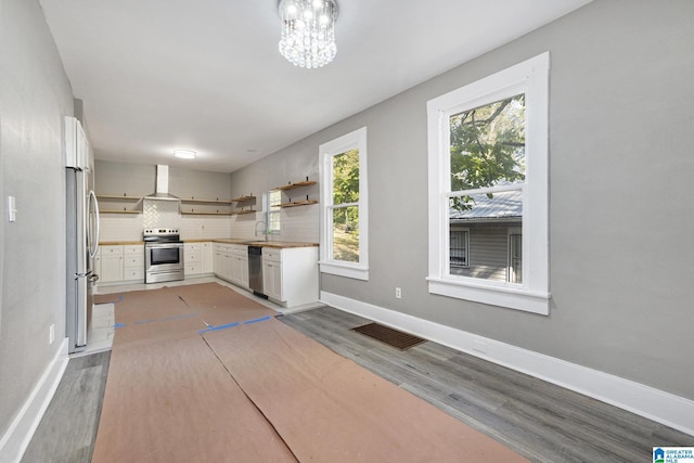 kitchen with wall chimney exhaust hood, stainless steel appliances, backsplash, a chandelier, and white cabinets