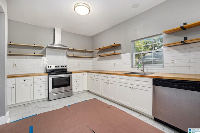 kitchen with wood counters, white cabinets, wall chimney range hood, sink, and stainless steel appliances