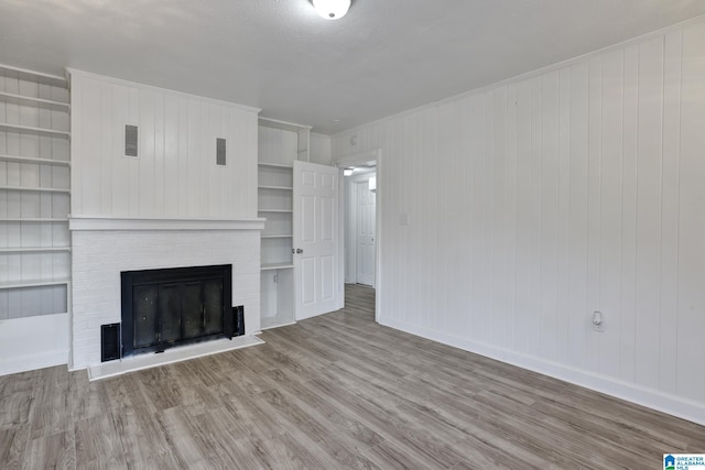 unfurnished living room featuring built in shelves, light hardwood / wood-style flooring, wooden walls, and a brick fireplace