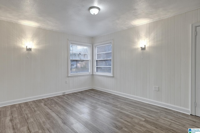 empty room with hardwood / wood-style floors, a textured ceiling, and wood walls