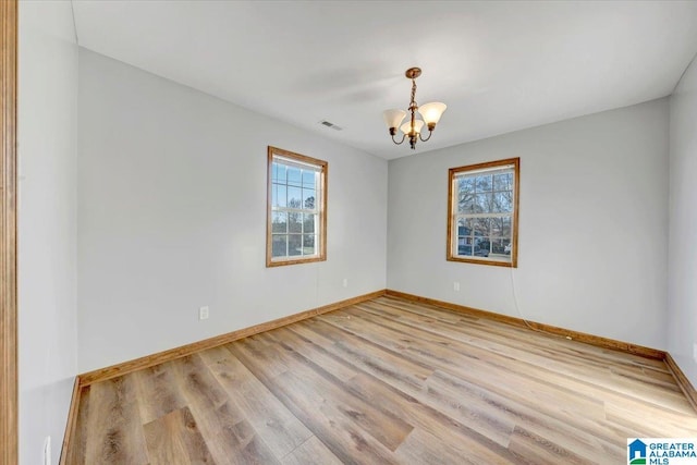 empty room with light wood-type flooring and a notable chandelier