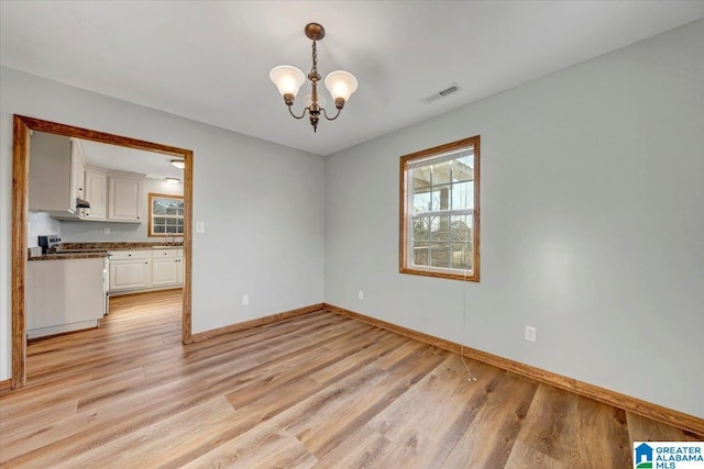 unfurnished room with light wood-type flooring and an inviting chandelier