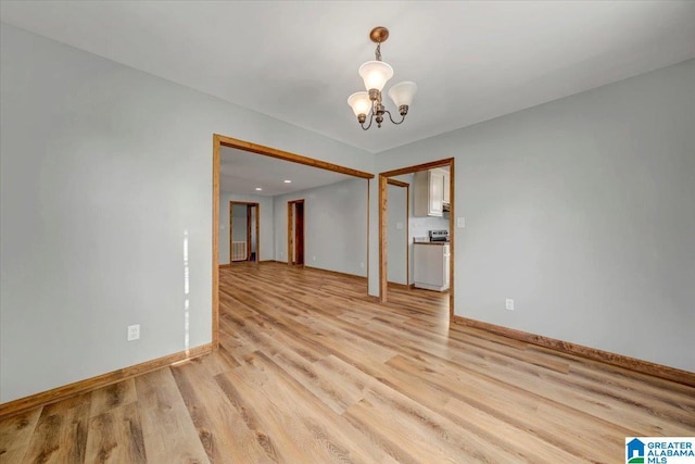 spare room featuring light wood-type flooring and a notable chandelier