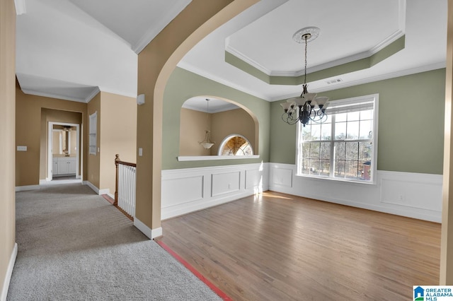 unfurnished dining area featuring a chandelier, a tray ceiling, crown molding, and light hardwood / wood-style floors