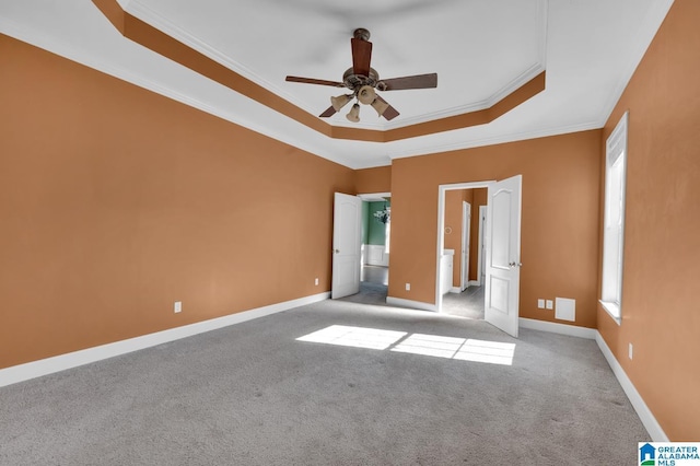 unfurnished bedroom with ceiling fan, ornamental molding, a tray ceiling, multiple windows, and light colored carpet