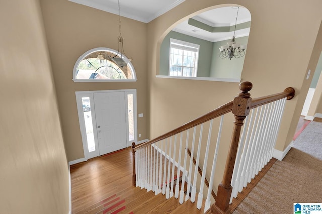 entryway with hardwood / wood-style floors, a raised ceiling, ornamental molding, and a notable chandelier