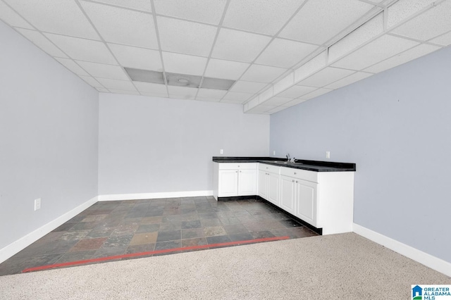 kitchen with dark colored carpet, a drop ceiling, white cabinetry, and sink