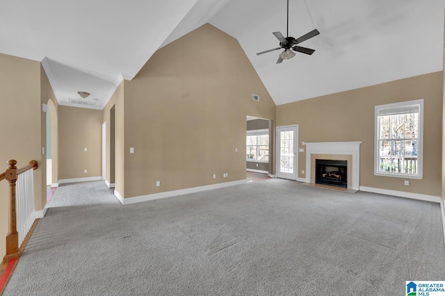 unfurnished living room with a wealth of natural light, ceiling fan, light colored carpet, and high vaulted ceiling