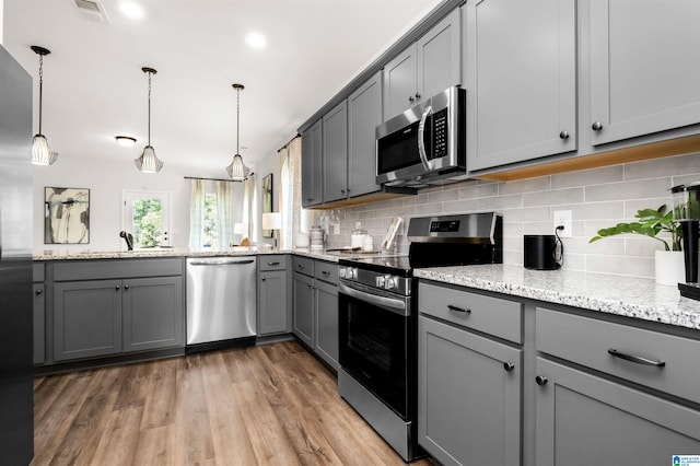 kitchen with gray cabinetry, hanging light fixtures, tasteful backsplash, wood-type flooring, and appliances with stainless steel finishes