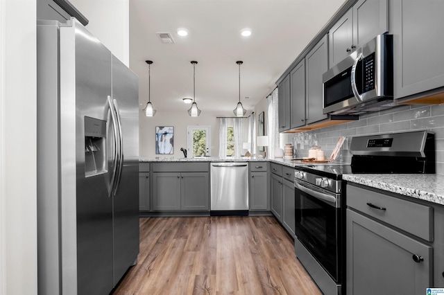 kitchen with backsplash, gray cabinets, light stone counters, and appliances with stainless steel finishes