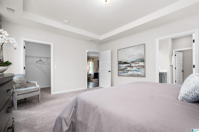 carpeted bedroom featuring a raised ceiling, a walk in closet, connected bathroom, and a closet