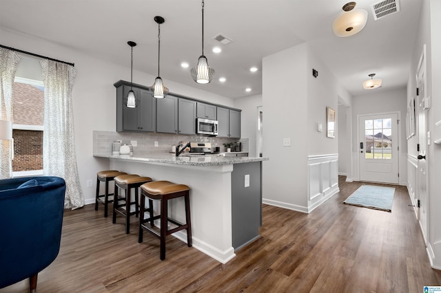 kitchen with gray cabinetry, hanging light fixtures, stainless steel appliances, kitchen peninsula, and decorative backsplash