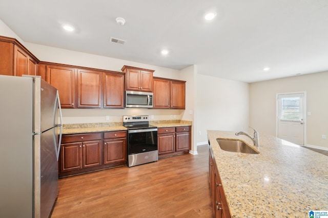 kitchen featuring hardwood / wood-style floors, light stone counters, sink, and stainless steel appliances