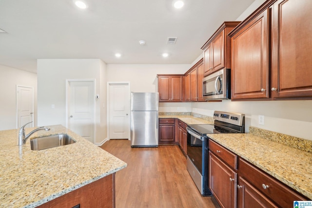 kitchen with light stone countertops, appliances with stainless steel finishes, light wood-type flooring, and sink