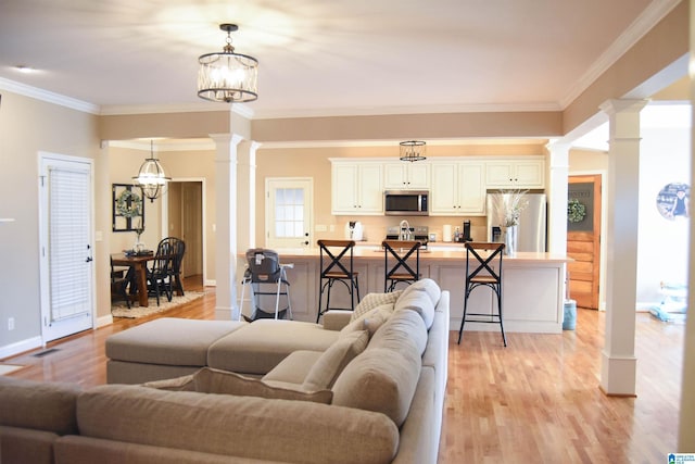 living room with light hardwood / wood-style floors, ornate columns, ornamental molding, and a chandelier