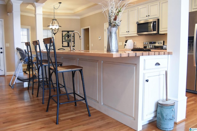 kitchen with pendant lighting, a kitchen bar, ornamental molding, and stainless steel appliances