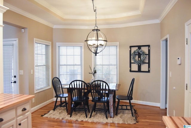 dining room featuring a tray ceiling, crown molding, light hardwood / wood-style flooring, and a notable chandelier