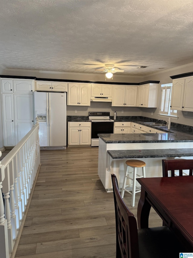 kitchen featuring kitchen peninsula, white appliances, dark wood-type flooring, white cabinetry, and a breakfast bar area