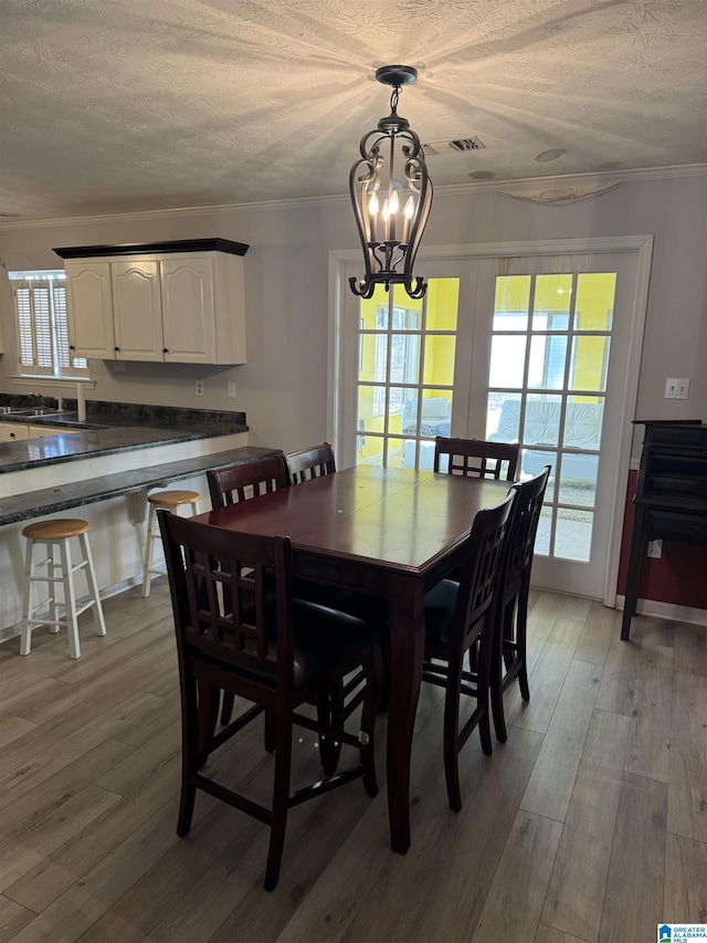 dining area with a chandelier, a textured ceiling, light hardwood / wood-style flooring, and crown molding