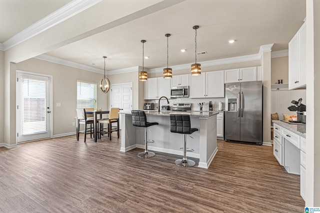 kitchen with light stone countertops, stainless steel appliances, pendant lighting, a kitchen island with sink, and white cabinets