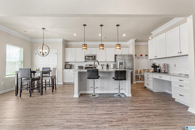 kitchen with white cabinets, an island with sink, decorative light fixtures, a kitchen bar, and stainless steel appliances