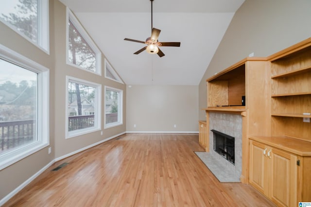 unfurnished living room featuring ceiling fan, a fireplace, a high ceiling, and light hardwood / wood-style flooring