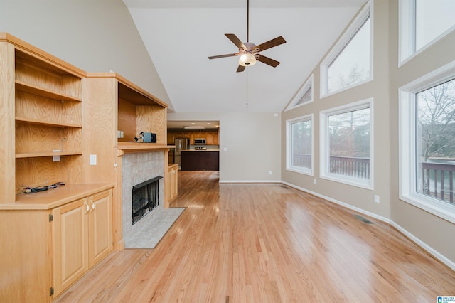 unfurnished living room featuring ceiling fan, a fireplace, high vaulted ceiling, and light hardwood / wood-style flooring