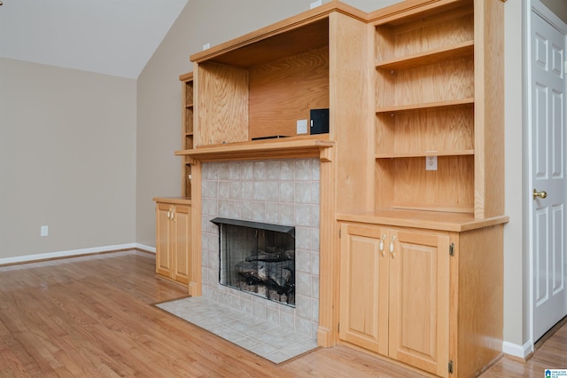 unfurnished living room featuring light hardwood / wood-style floors, lofted ceiling, and a tiled fireplace