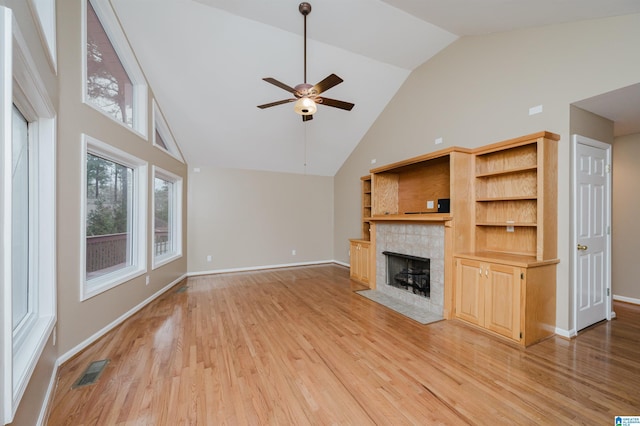 unfurnished living room with a tiled fireplace, ceiling fan, light hardwood / wood-style flooring, and high vaulted ceiling