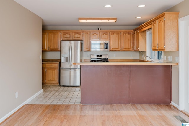 kitchen featuring kitchen peninsula, appliances with stainless steel finishes, light hardwood / wood-style floors, and sink