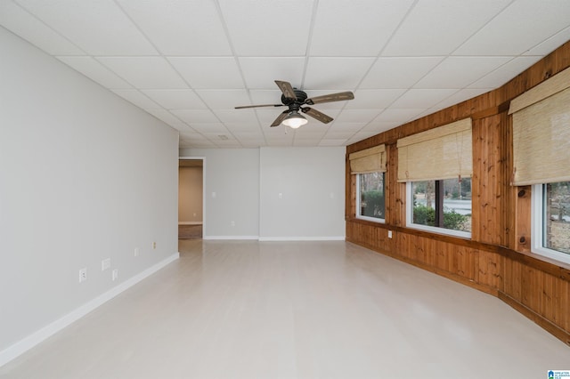 unfurnished room with a paneled ceiling, ceiling fan, and wood walls