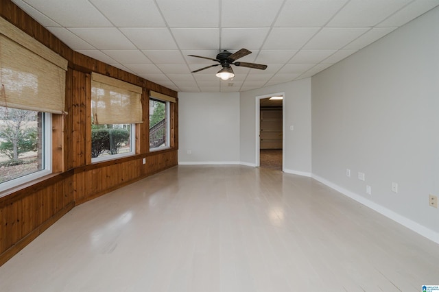 empty room featuring a paneled ceiling, ceiling fan, and wooden walls