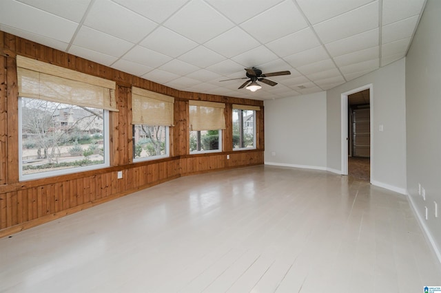 unfurnished room with a drop ceiling, wooden walls, and ceiling fan