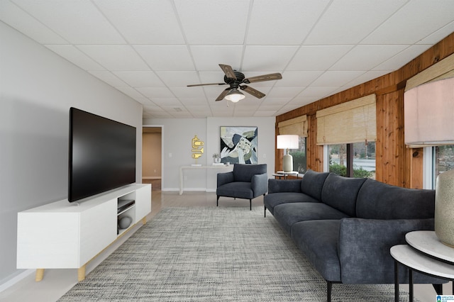 living room featuring ceiling fan, wood walls, and a drop ceiling