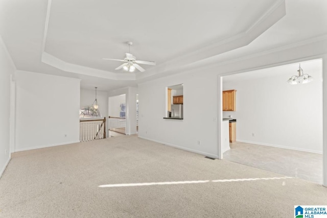 unfurnished living room with carpet flooring, ceiling fan with notable chandelier, and a raised ceiling