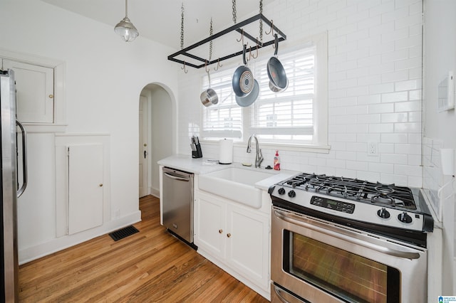 kitchen featuring appliances with stainless steel finishes, light wood-type flooring, sink, decorative light fixtures, and white cabinets