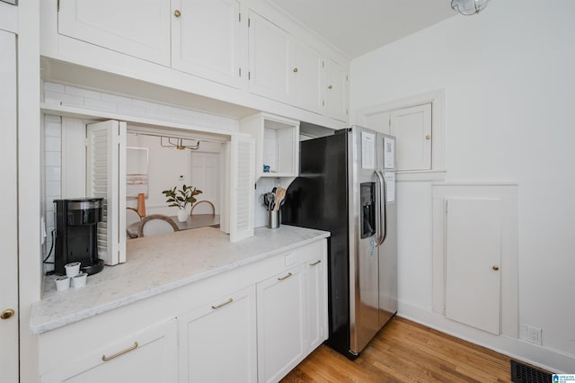 kitchen featuring light stone countertops, stainless steel fridge, white cabinets, and light hardwood / wood-style floors