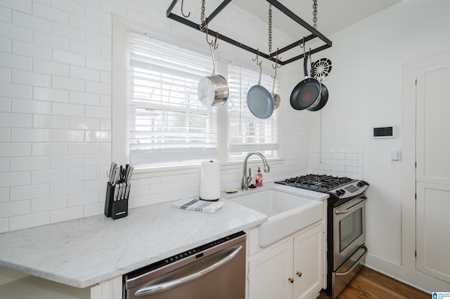 kitchen featuring light stone countertops, sink, white cabinetry, tasteful backsplash, and appliances with stainless steel finishes