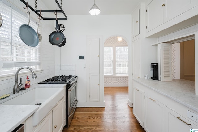 kitchen featuring hardwood / wood-style floors, hanging light fixtures, stainless steel gas stove, light stone countertops, and white cabinetry