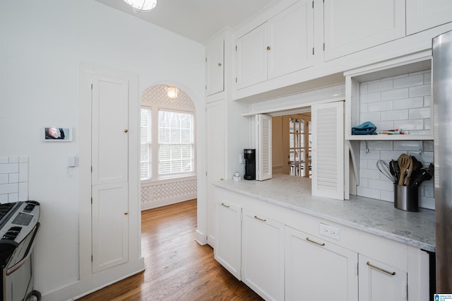 kitchen featuring white cabinets, wood-type flooring, backsplash, and light stone counters