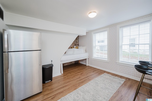 bedroom with stainless steel refrigerator, brick wall, and light wood-type flooring