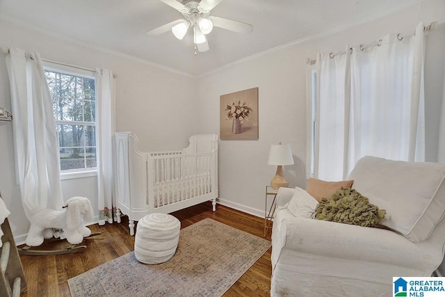 bedroom with ceiling fan, ornamental molding, dark wood-type flooring, and a nursery area