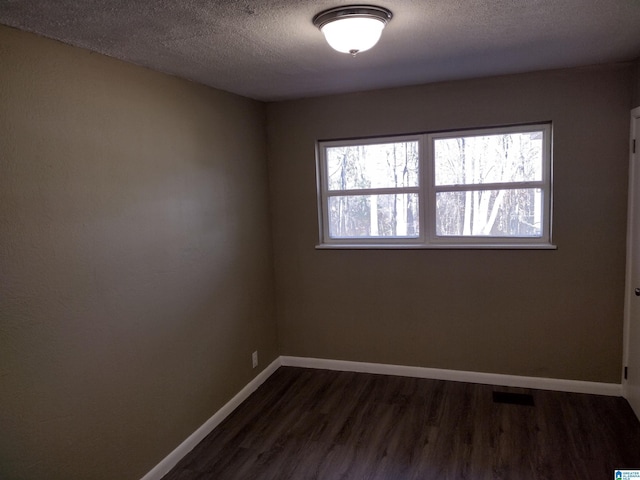 unfurnished room featuring dark wood-type flooring and a textured ceiling