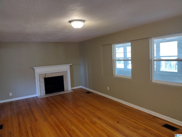 unfurnished living room featuring wood-type flooring, a premium fireplace, and a textured ceiling