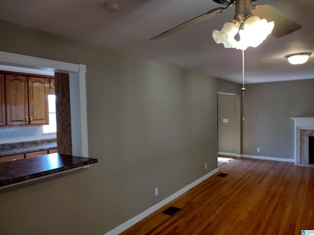 unfurnished dining area featuring hardwood / wood-style floors, ceiling fan, and a fireplace